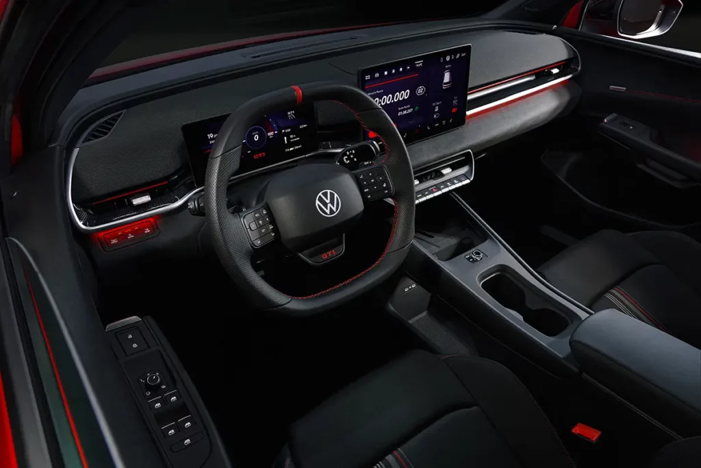 Vue de l'habitacle d'une Volkswagen ID. Polo GTI électrique avec le volant, l'écran central d'infodivertissement et des surpiqûres rouges et blanches.