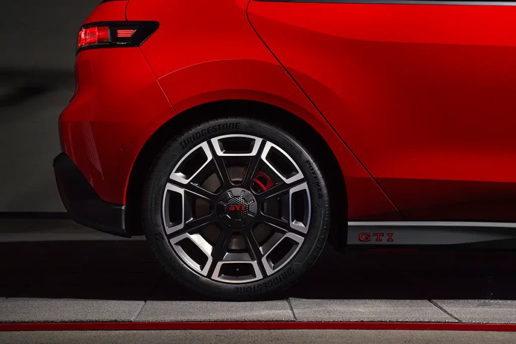 Gros plan de face sur la jante arrière 19 pouces avec logo GTI rouge au centre, dans un décor futuriste rouge et gris.