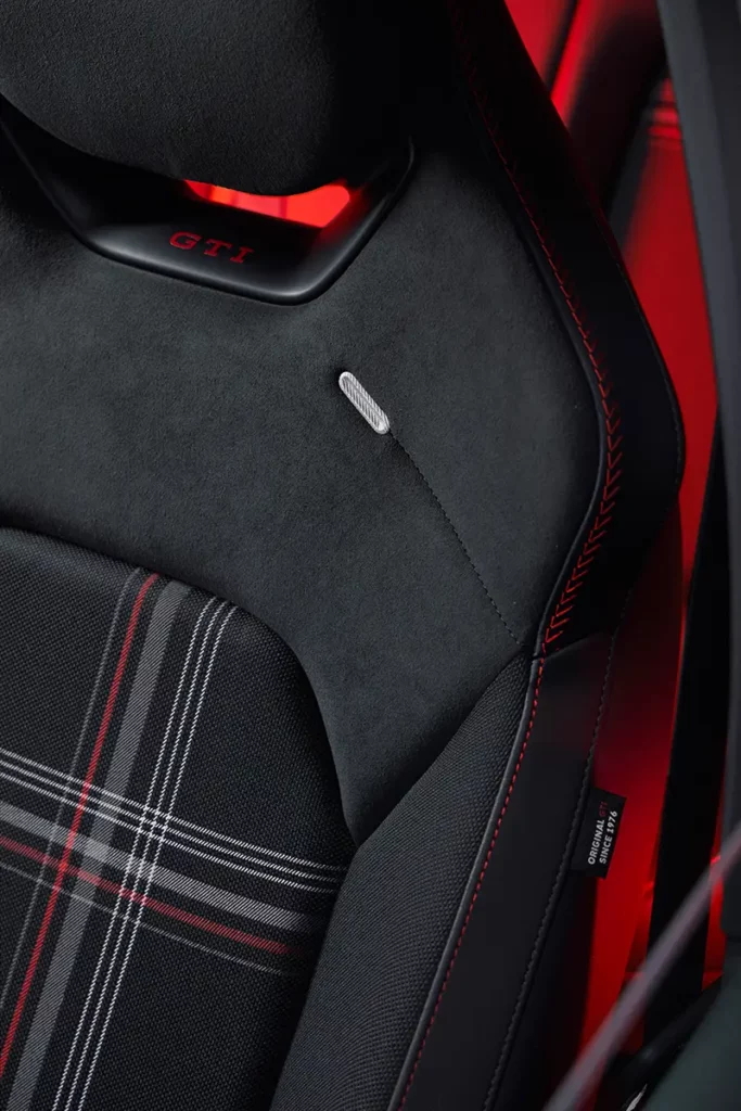 Gros plan sur les sièges sport en alcantara et tissu tartan d'une Volkswagen ID. Polo GTI électrique avec couture rouge et étiquette Original GTI since 1976.