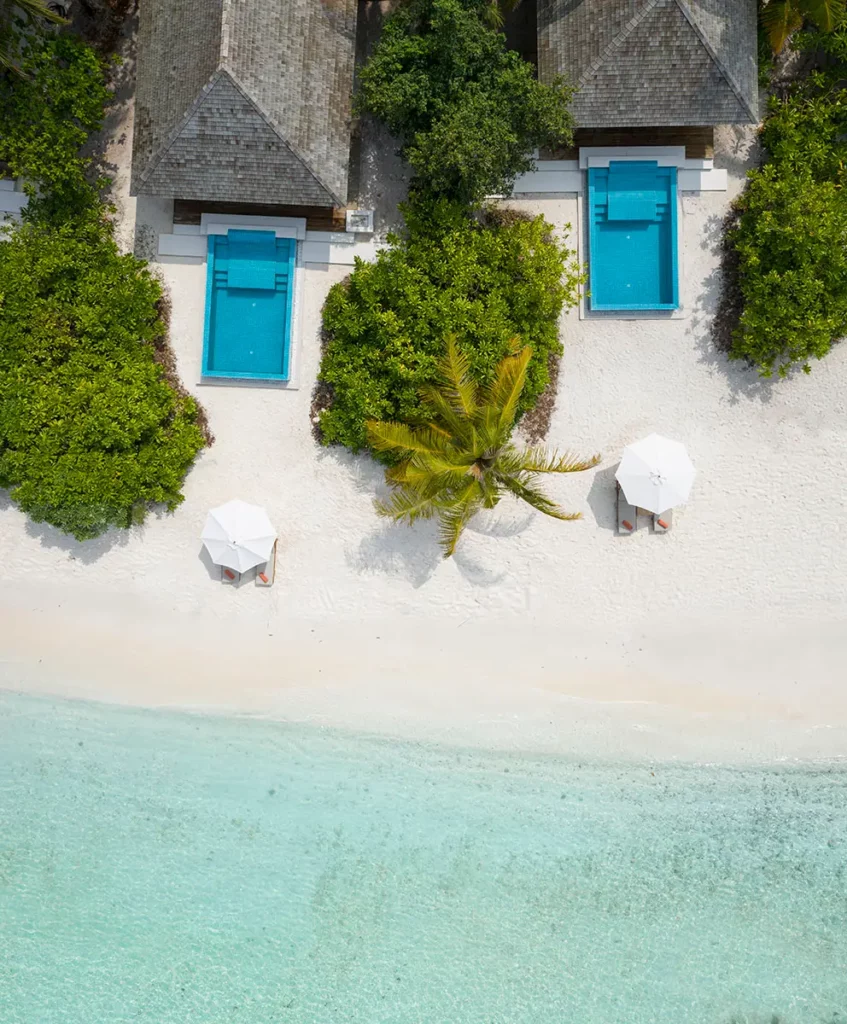 Vue aérienne verticale de deux Beach Villas avec toits de chaume et piscines privées sur le sable blanc bordé par la mer turquoise à Emerald Faarufushi.