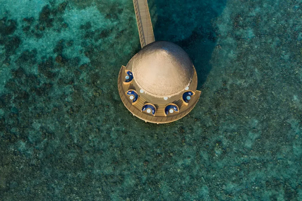 Vue aérienne du restaurant Boli à Emerald Faarufushi, sa structure arrondie et son ponton entourés par les eaux turquoises et les récifs coralliens du lagon.