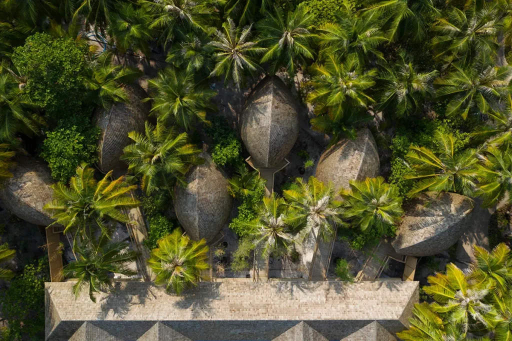 Vue aérienne en plongée totale des cabines du Spa Nika à Emerald Faarufushi, révélant leurs toits en forme de tortue nichés au cœur d'une palmeraie dense.