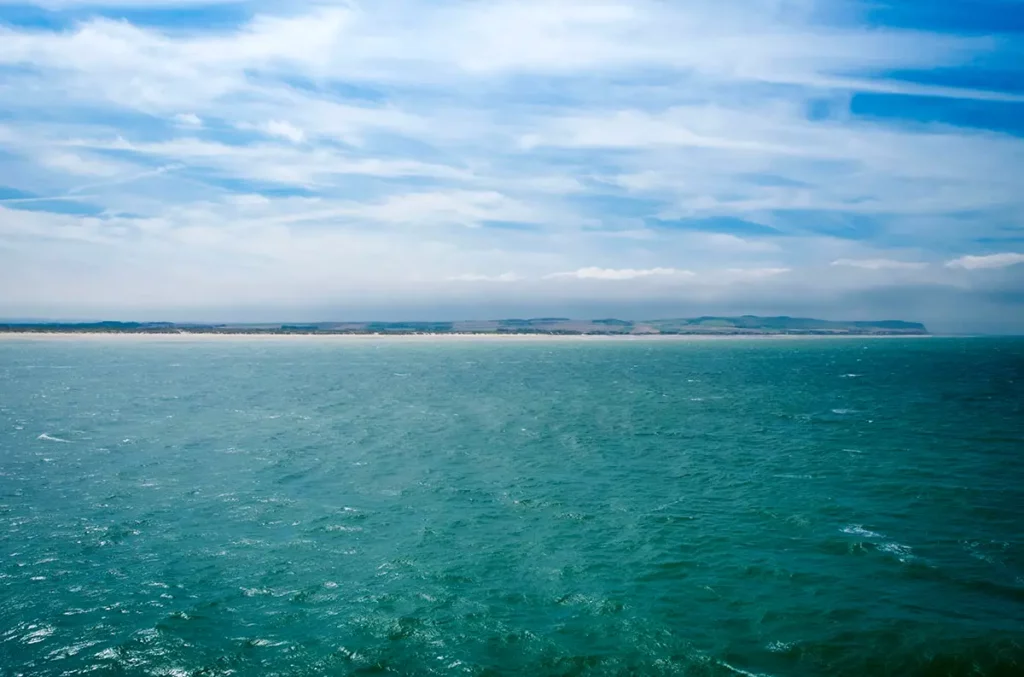 Fine ligne horizontale des côtes françaises et des plages de Calais s’éloignant en mer du Nord sous un ciel bleu de printemps.