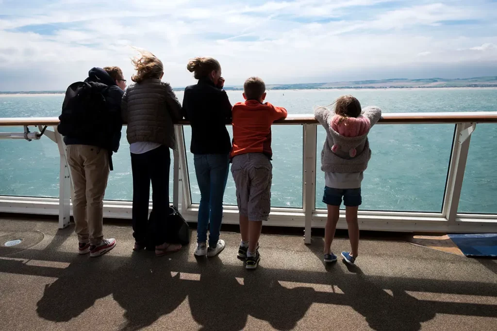 Famille de dos sur le pont d'un bateau P&O Ferries regarde les côtes françaises s'éloigner derrière le garde-corps en verre.