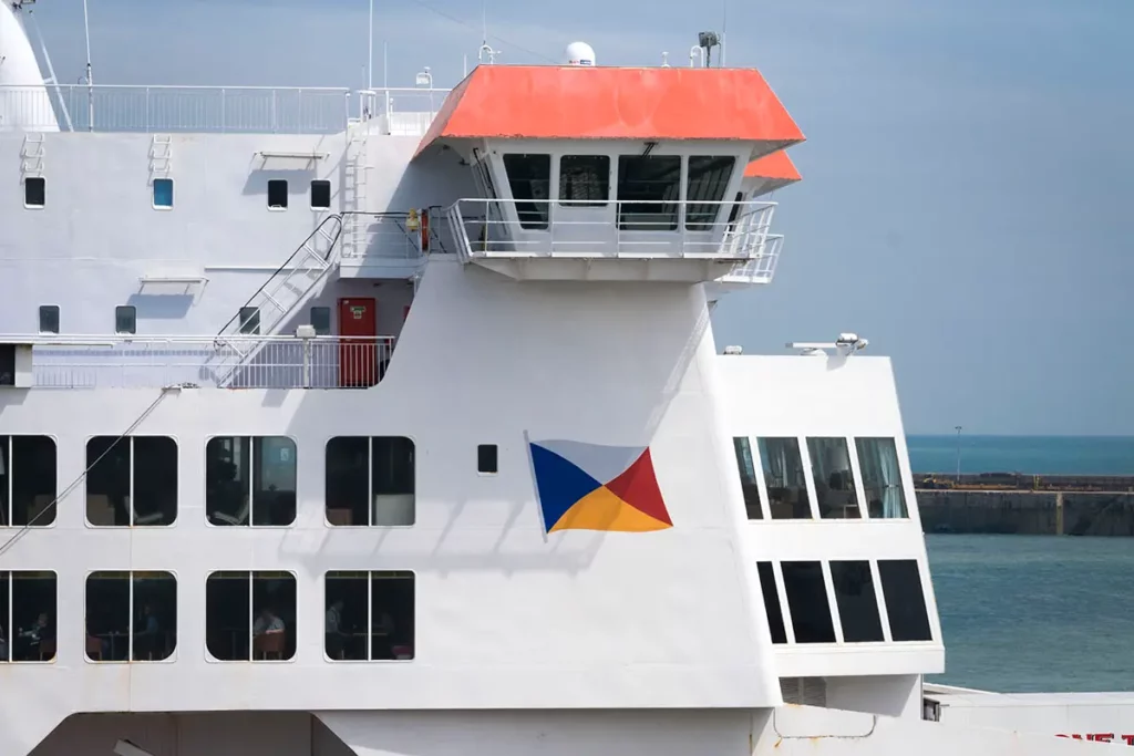 Gros plan sur la timonerie d'un ferry P&O avec son toit orange, ses fenêtres carrées et rectangulaires, et le logo de la compagnie sur l'acier blanc.