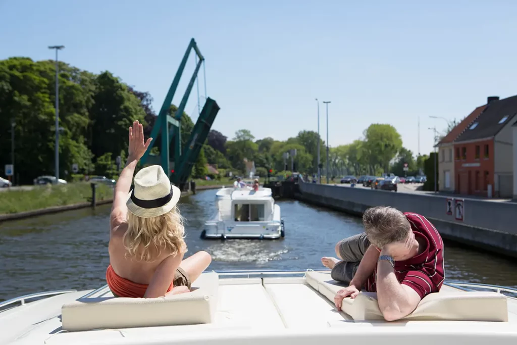 Un couple de dos se détend sur le pont avant d'un bateau Le Boat en Belgique, alors qu'un pont-levis se lève sur le canal pour laisser passer l'embarcation.