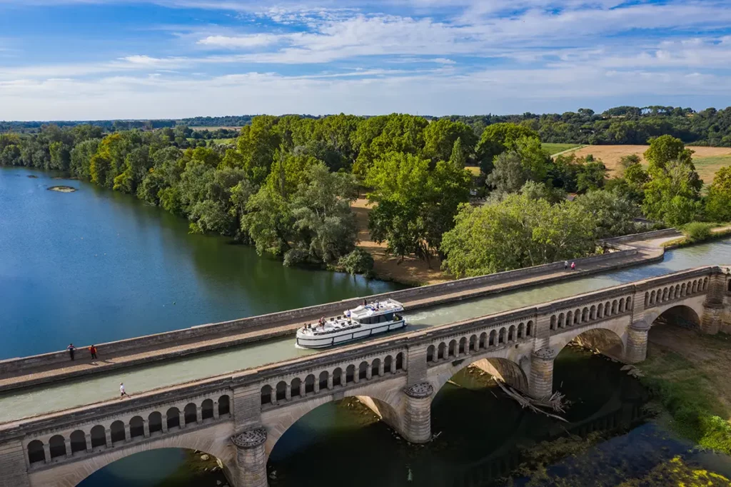 Vue d'un bateau Le Boat franchissant un pont-canal typique du Canal du Midi dans le sud de la France, un ouvrage d'art historique qui enjambe un fleuve.