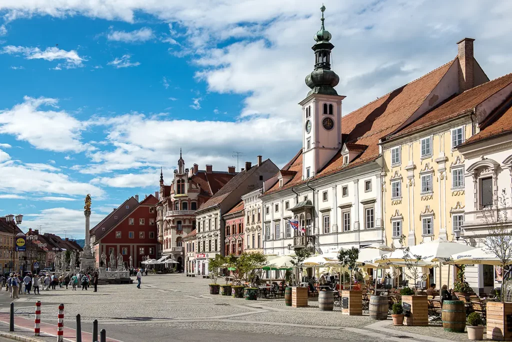 Place centrale de Maribor lors d'un road-trip en Slovénie, montrant les façades colorées, l'hôtel de ville au clocher blanc et la colonne de la peste surmontée d'une statue dorée.