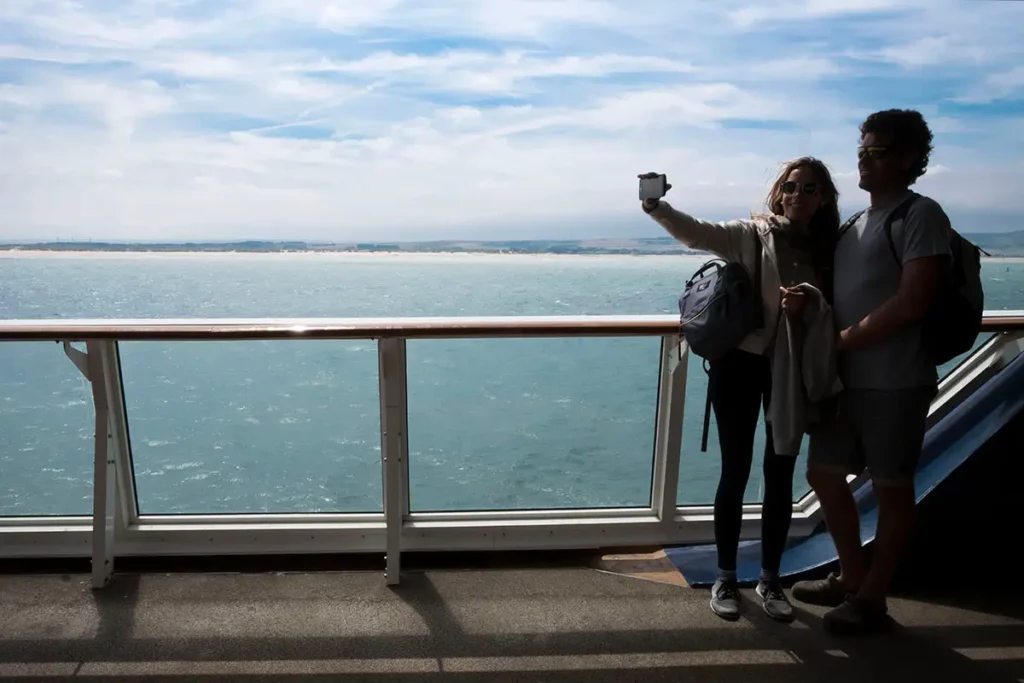 Deux personnes se prenant en selfie sur le pont du ferry P&O avec la mer et la côte française qui s'éloigne en arrière-plan.