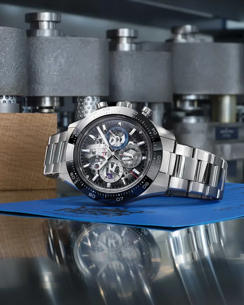 Montre Zenith Chronomaster Sport Skeleton en acier allongée sur un support bleu avec reflet sur la table dans un atelier horloger.