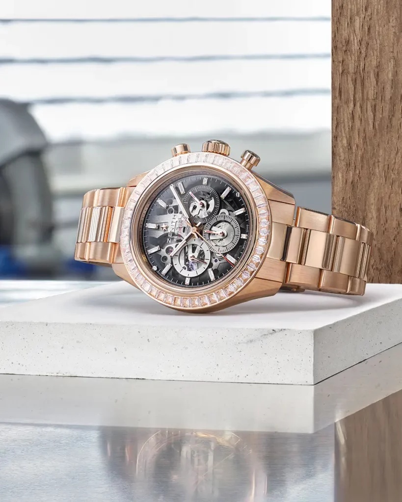 Édition limitée de la montre Zenith Chronomaster Sport Skeleton en or rose et diamants couchée sur un socle en pierre blanche et une plaque métallique réfléchissante.
