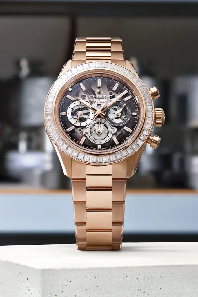 Édition limitée de la montre Zenith Chronomaster Sport Skeleton en or rose avec lunette sertie de diamants taille baguette, de face sur un socle en pierre blanche.