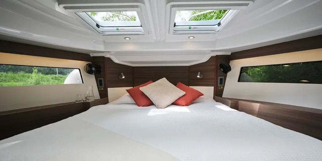 Cabine avant lumineuse avec lit double et finitions en boiseries à bord du bateau Liberty Le Boat, alliant confort moderne et atmosphère cosy.