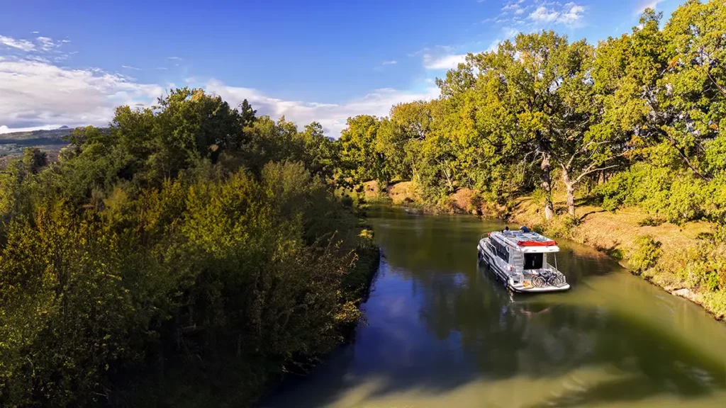 Croisière Le Boat avec un bateau Liberty naviguant dans un virage du canal du Midi en automne, avec des vélos installés à l'arrière pour les excursions.