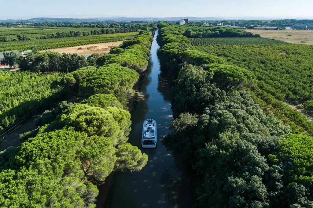 Bateau Le Boat naviguant sur le canal du Midi à Sallèles-d'Aude, avec un couple se relaxant sur le pont avant et le pilote à la barre extérieure.