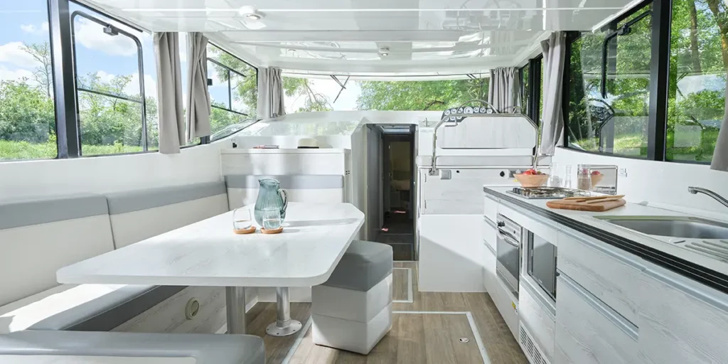 Espace de vie lumineux avec salon et cuisine moderne à bord d'un bateau Le Boat Horizon 5, offrant une vue panoramique sur les canaux.