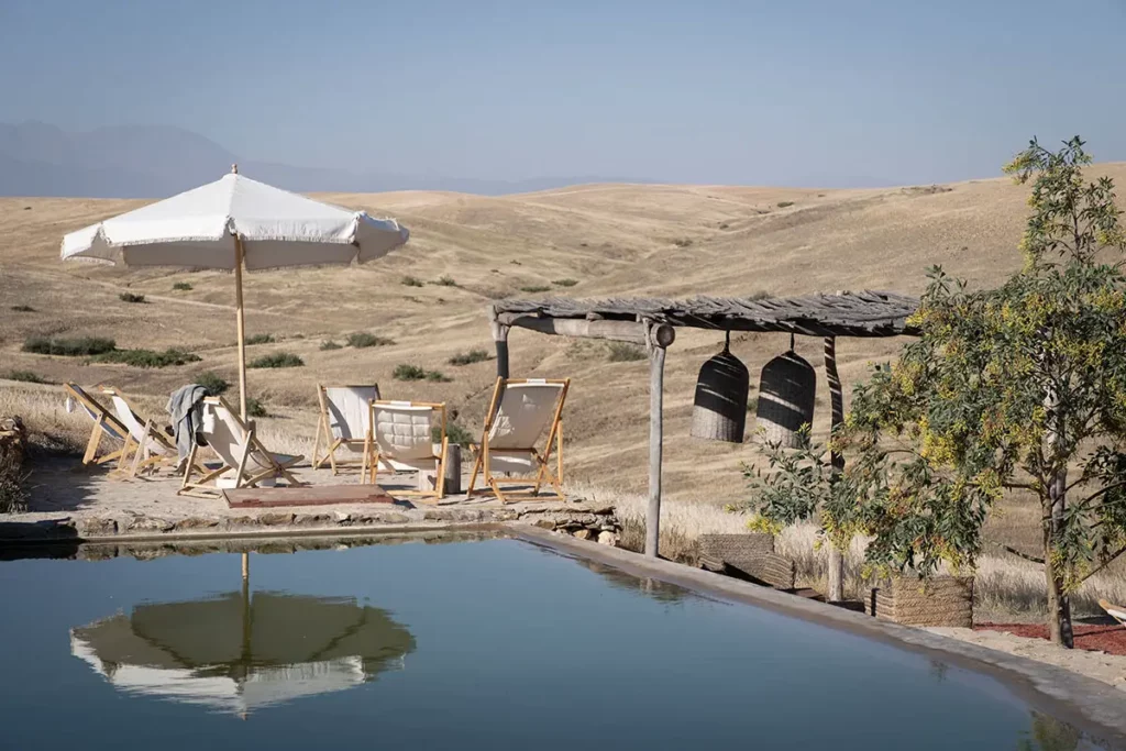 Piscine et végétation de l'oasis face aux collines du désert d'Agafay à Terre des Étoiles