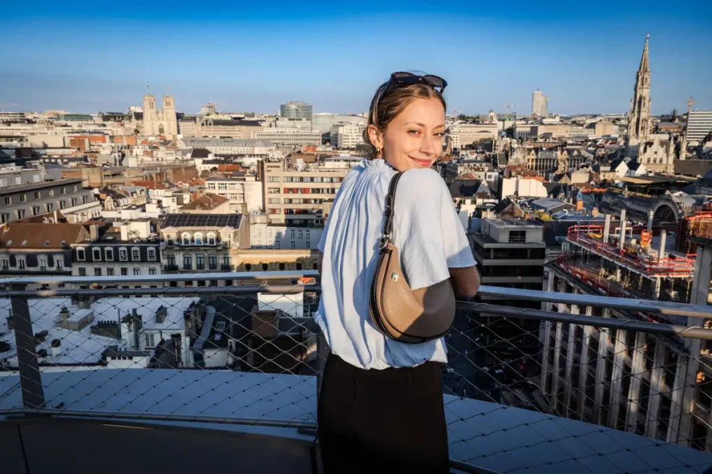 Portrait horizontal au grand-angle d'une jeune femme se retournant sur le rooftop 58 face au panorama est de Bruxelles au coucher du soleil