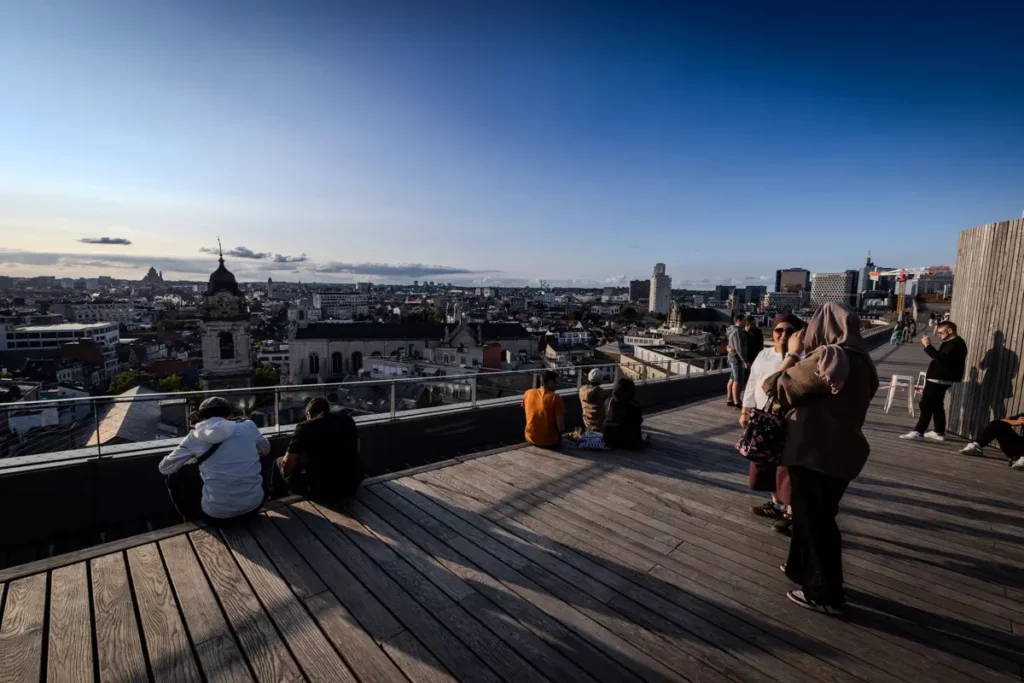 Vue grand-angle de la grande terrasse en bois du rooftop 58 au coucher du soleil avec panorama sur Bruxelles