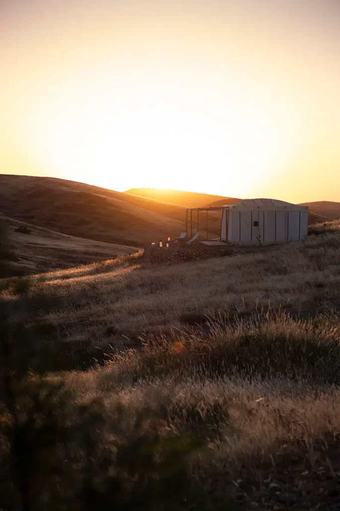 Tente nomade éclairée à contre-jour par le coucher du soleil sur les collines du désert d'Agafay à Terre des Étoiles