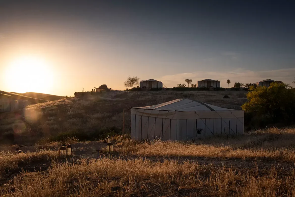 Tentes lodge nomades éclairées à contre-jour par le coucher du soleil au domaine Terre des Étoiles dans le désert d'Agafay