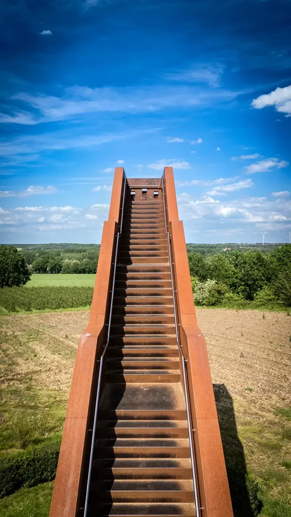 Vue verticale de la Vlooybergtoren par drone à mi-hauteur montrant la perspective des marches menant vers le ciel bleu