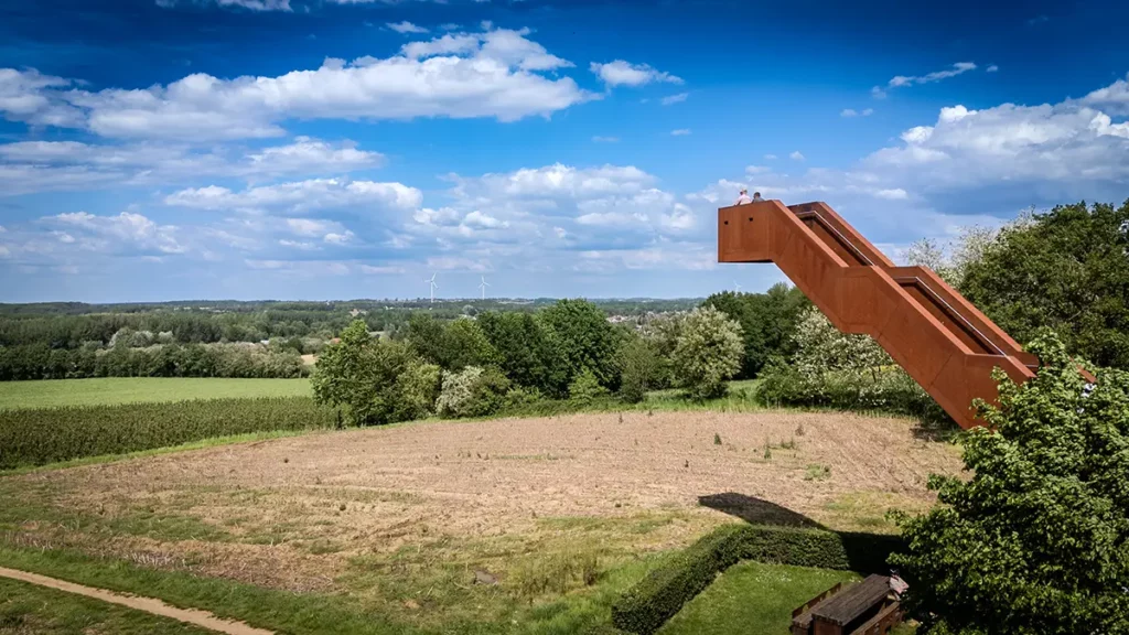 Vue éloignée et basse de la Vlooybergtoren avec des visiteurs à son sommet un homme assis sur un banc et deux éoliennes au loin