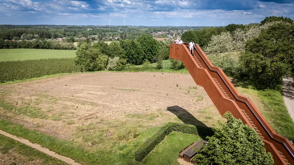 Vue éloignée au drone de la Vlooybergtoren dans le paysage du Hageland montrant des visiteurs à son sommet et des éoliennes à l'horizon