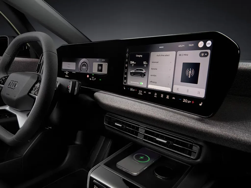 Gros plan sur le double écran panoramique MMI et le tableau de bord numérique de l'Audi A2 e-tron, affichant les menus de recharge et de conduite