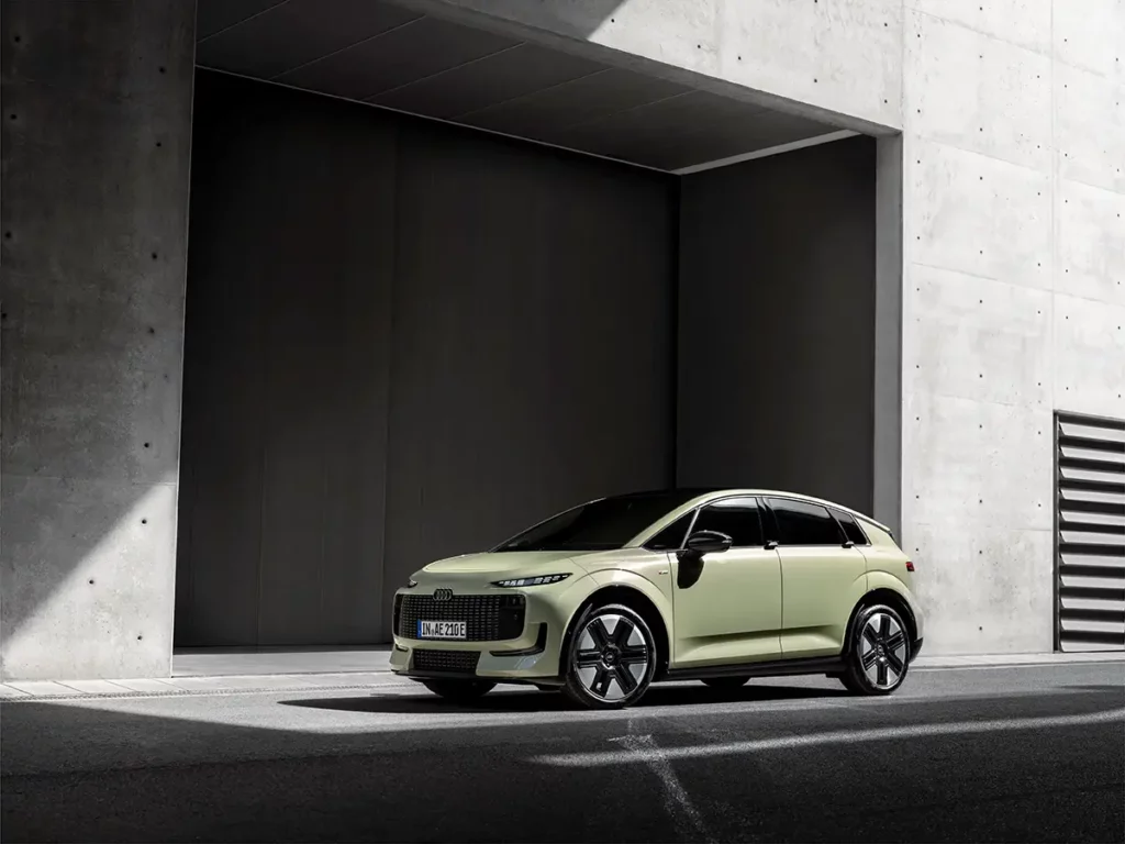 Vue de trois-quarts avant de l'Audi A2 e-tron sous un éclairage contrasté, mettant en valeur sa face avant et ses projecteurs LED face à une architecture en béton ombragée