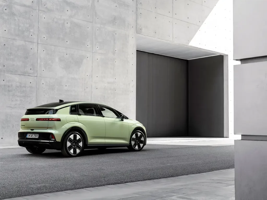 Vue de trois-quarts arrière droit de la nouvelle Audi A2 e-tron de couleur vert mint, montrant sa signature lumineuse et son hayon devant un mur en béton