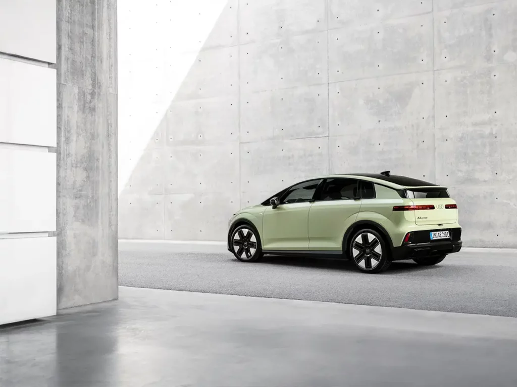 Vue de trois-quarts arrière gauche de la nouvelle Audi A2 e-tron de couleur vert mint, stationnée devant un bâtiment en béton à Ingolstadt. On distingue le hayon et la signature lumineuse arrière