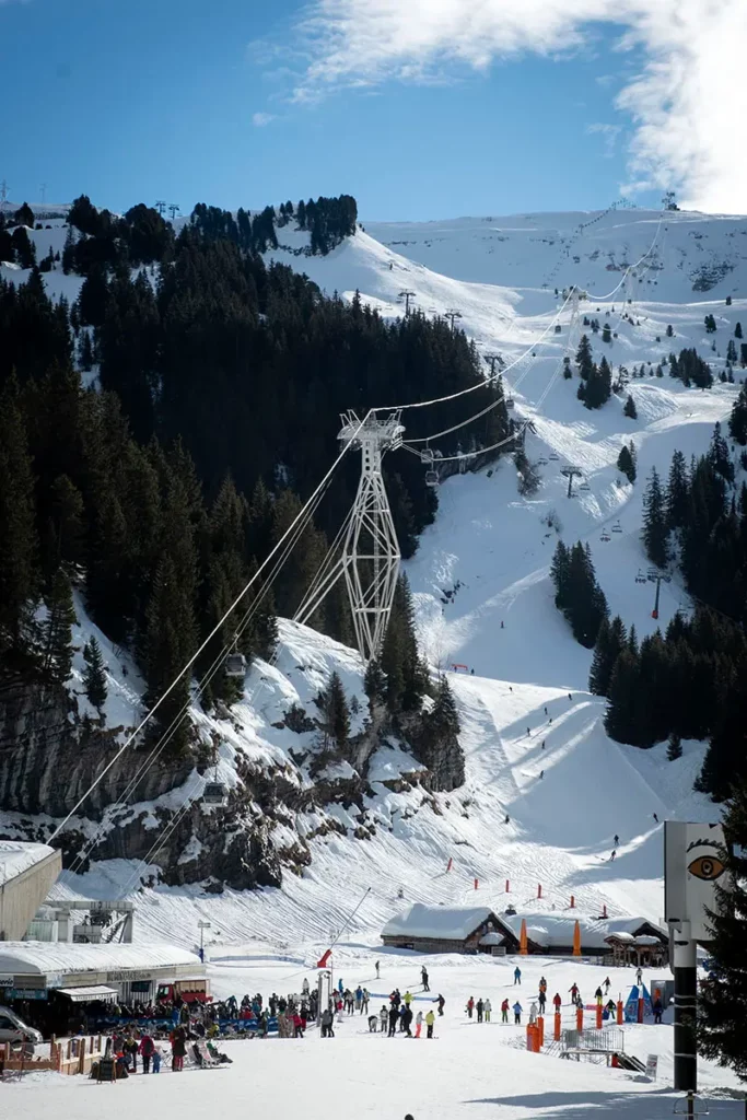 Photo verticale du front de neige de Flaine montrant le départ des télécabines au pied des immeubles et des skieurs dévalant la piste à toute vitesse