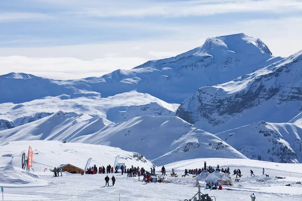 Vue panoramique d'un site d'activités avec des visiteurs face aux sommets enneigés d'Orcières Merlette 1850 dans les Hautes-Alpes