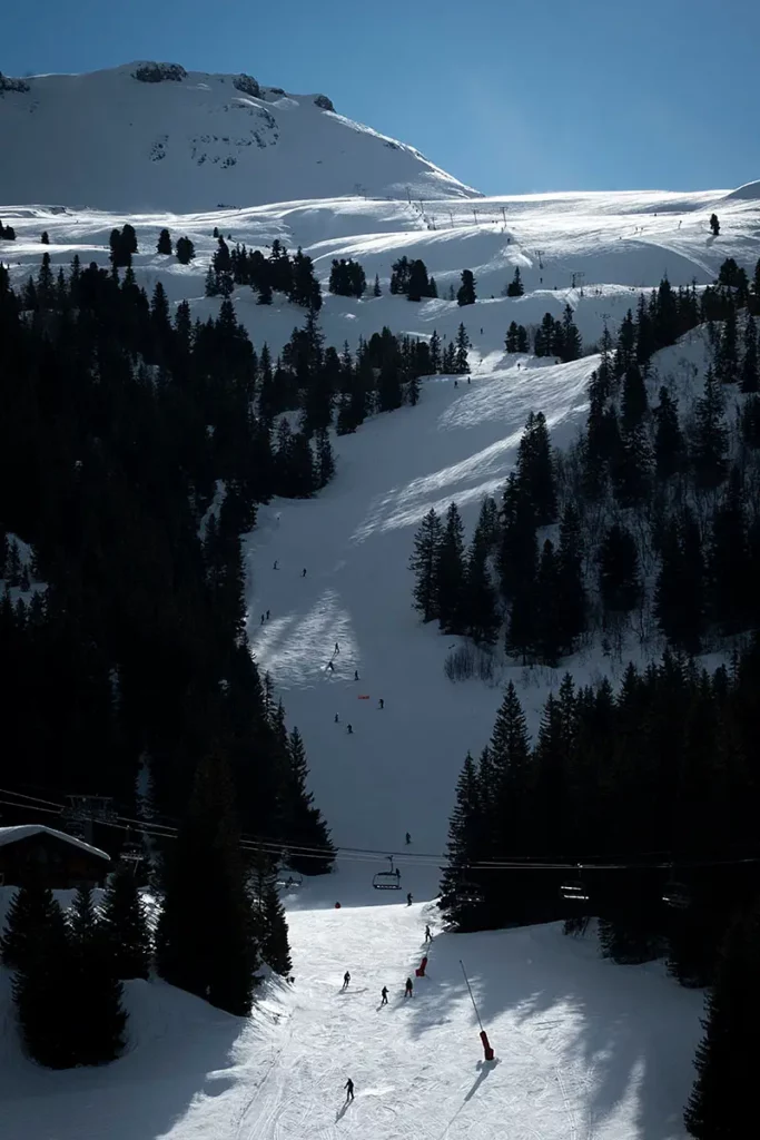 Photo verticale de la piste de ski descendant face au front de neige à Flaine prise au téléobjectif avec une lumière rasante et de nombreux skieurs