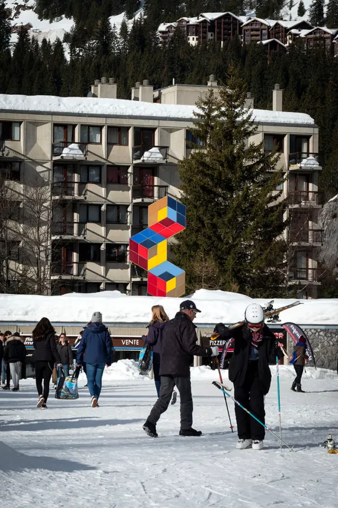 scène de vie animée sur le front de neige de Flaine avec la sculpture monumentale de l'artiste Victor Vasarely au centre et les bâtiments Bauhaus en arrière-plan