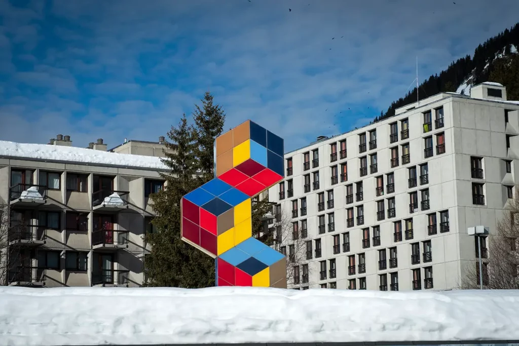 Photo verticale montrant la sculpture colorée de Victor Vasarely dressée comme un totem au milieu des bâtiments en béton de style Bauhaus à Flaine