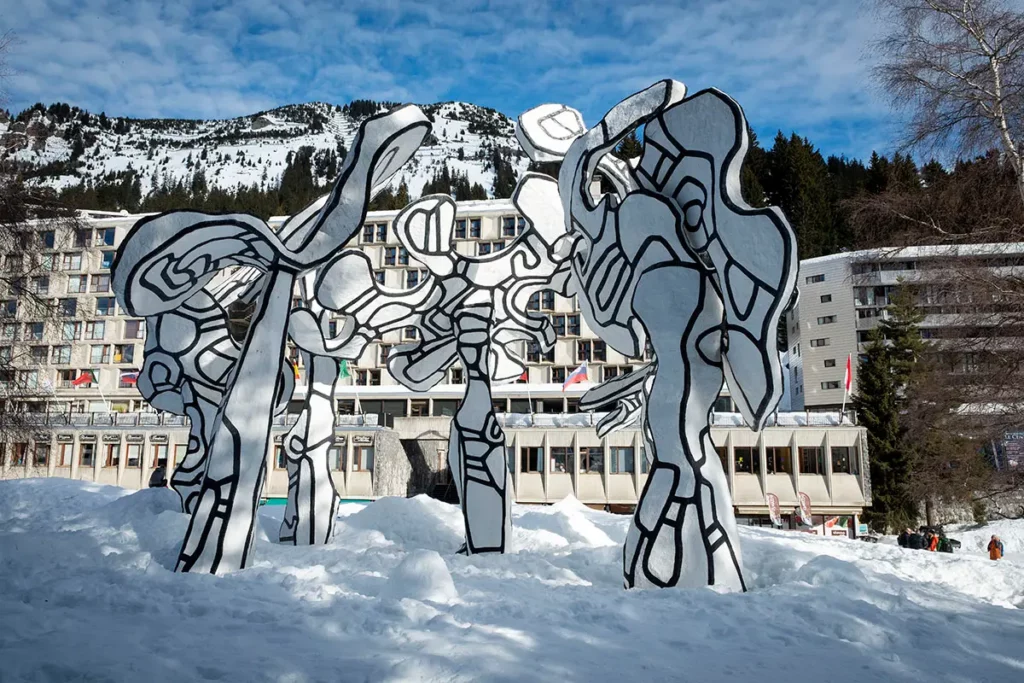 Photo horizontale montrant la vue complète de l'œuvre Les Hourloupes de Jean Dubuffet posée sur la neige à Flaine, avec les structures Bauhaus et les montagnes en arrière-plan