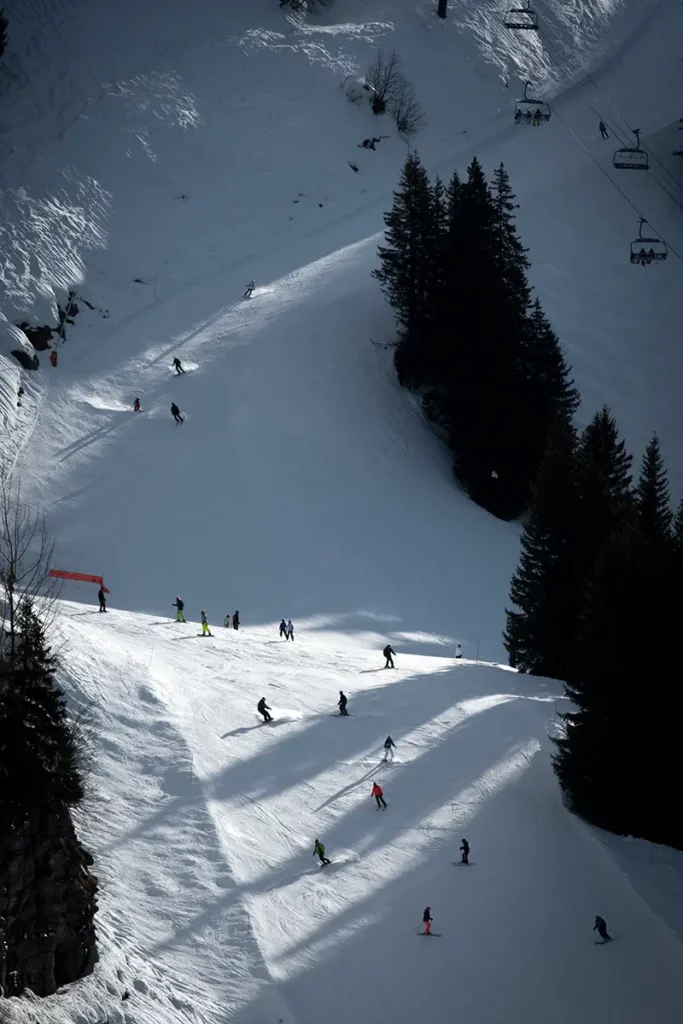photo verticale prise au téléobjectif montrant une multitude de skieurs dévalant la piste en fin d'après-midi sur le front de neige de Flaine avec des contrastes de lumière marqués