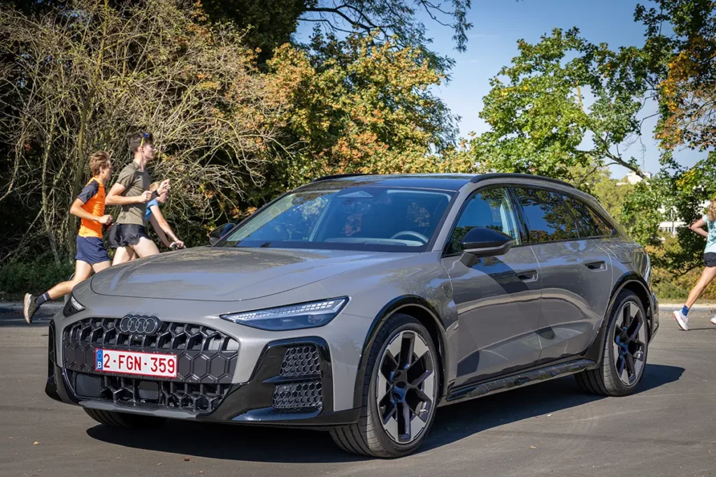 L'Audi A6 allroad e-hybrid photographiée en milieu urbain verdoyant lors de mon essai automobile en Belgique, avec des coureurs en arrière-plan