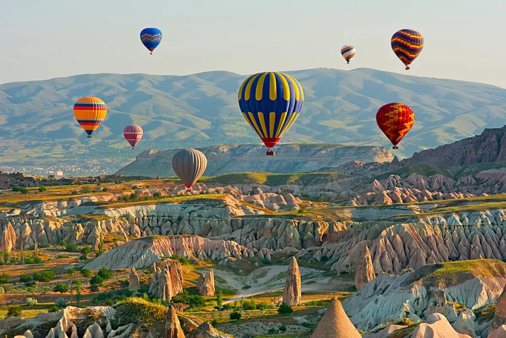 Montgolfières colorées survolant les cheminées de fées et les vallées rocheuses de la Cappadoce au lever du soleil avec Go Türkiye